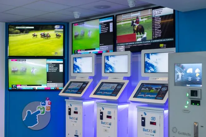 Self-service betting terminals, race screens and a cash machine on a betting shop floor
